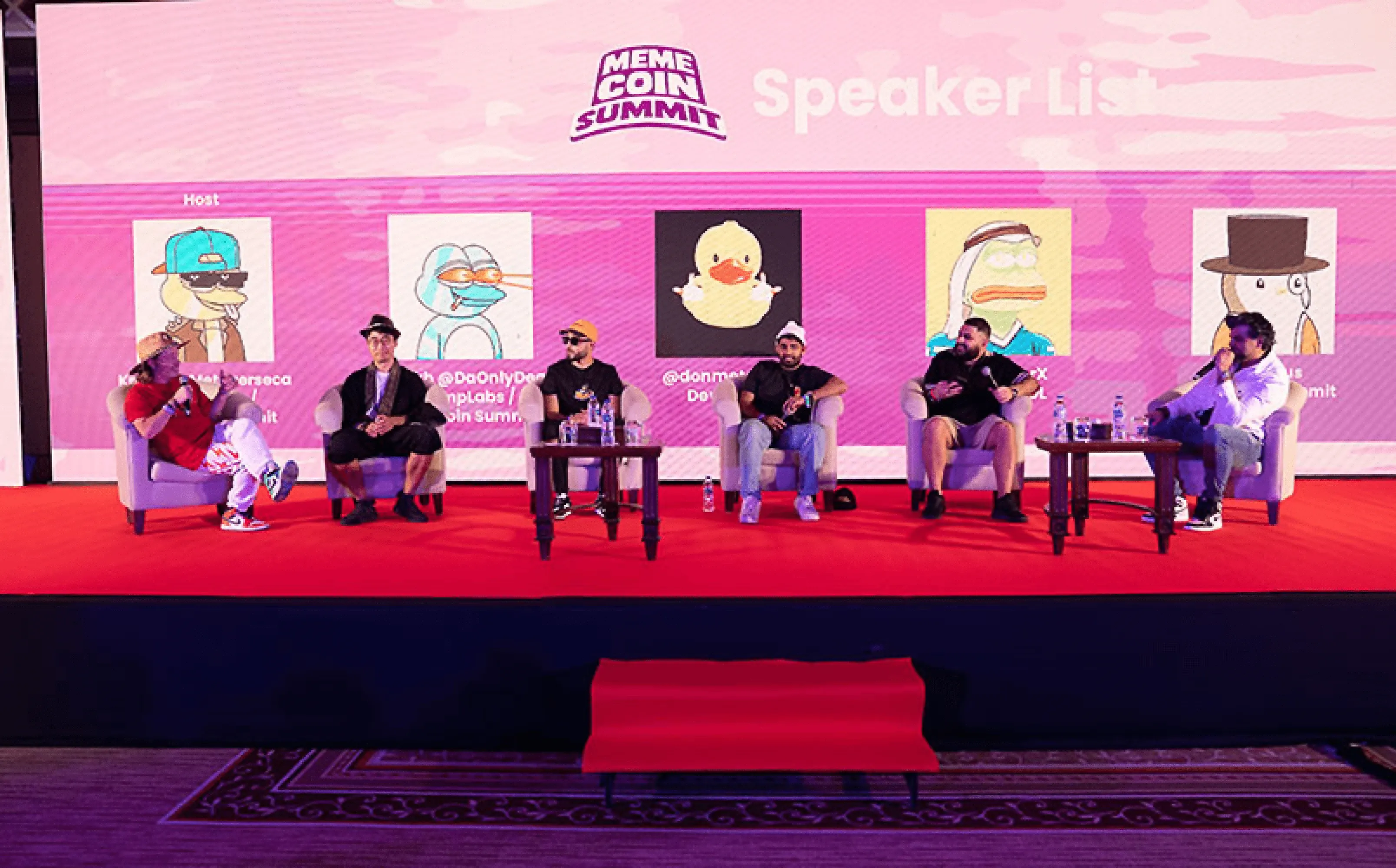 MemeCoin Summit 2024 – Panel discussion featuring industry experts on a red-carpeted stage with a vibrant backdrop of speaker avatars.